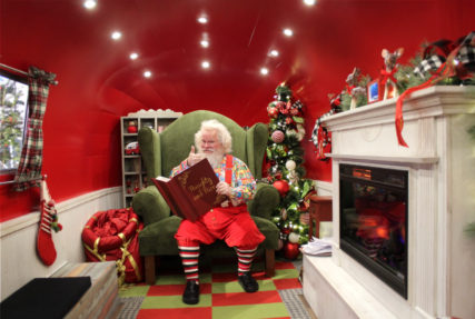 Santa is sitting in his chair inside Airstream with Naughty and Nice Book in his hands