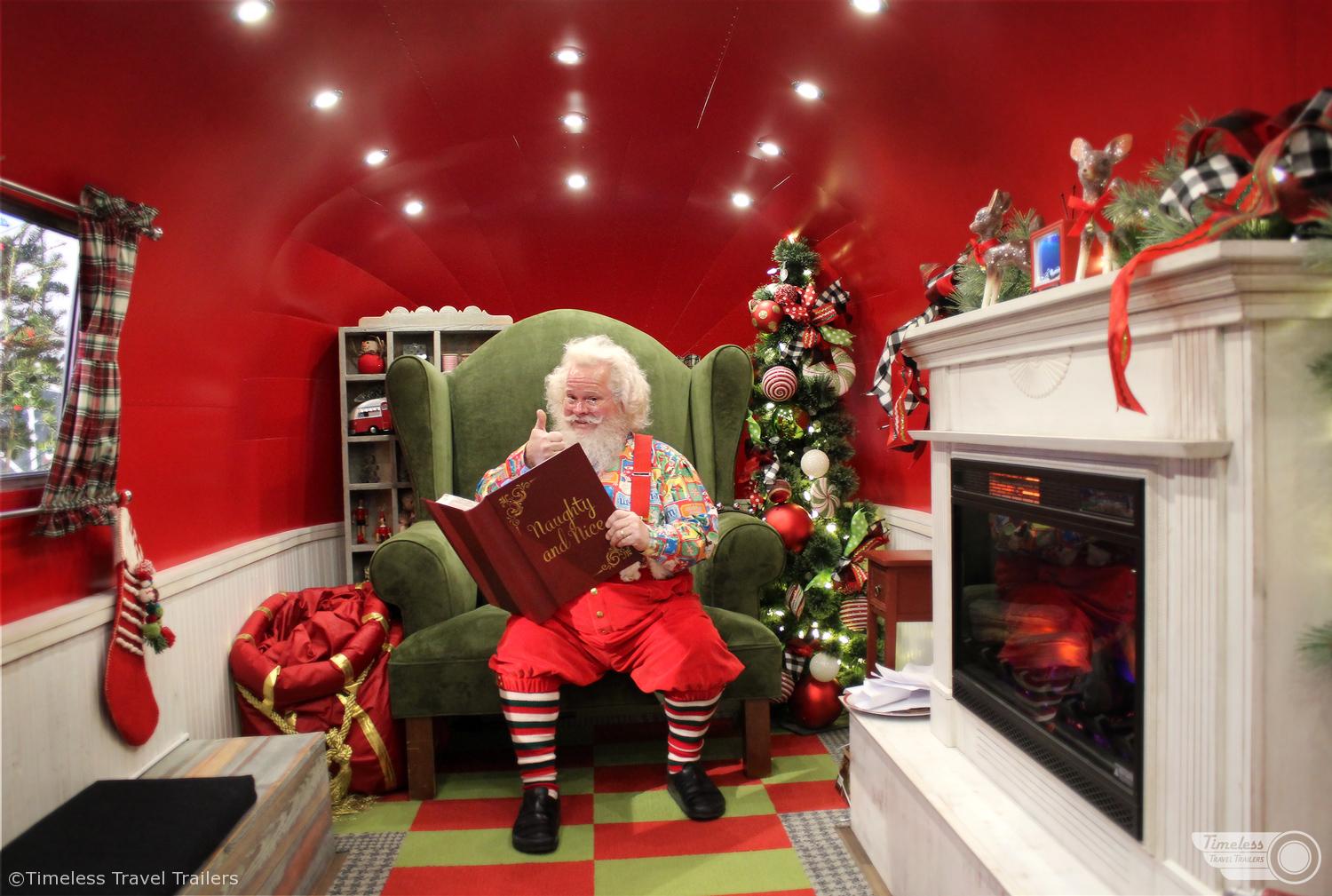Santa is sitting in his chair inside Airstream with Naughty and Nice Book in his hands